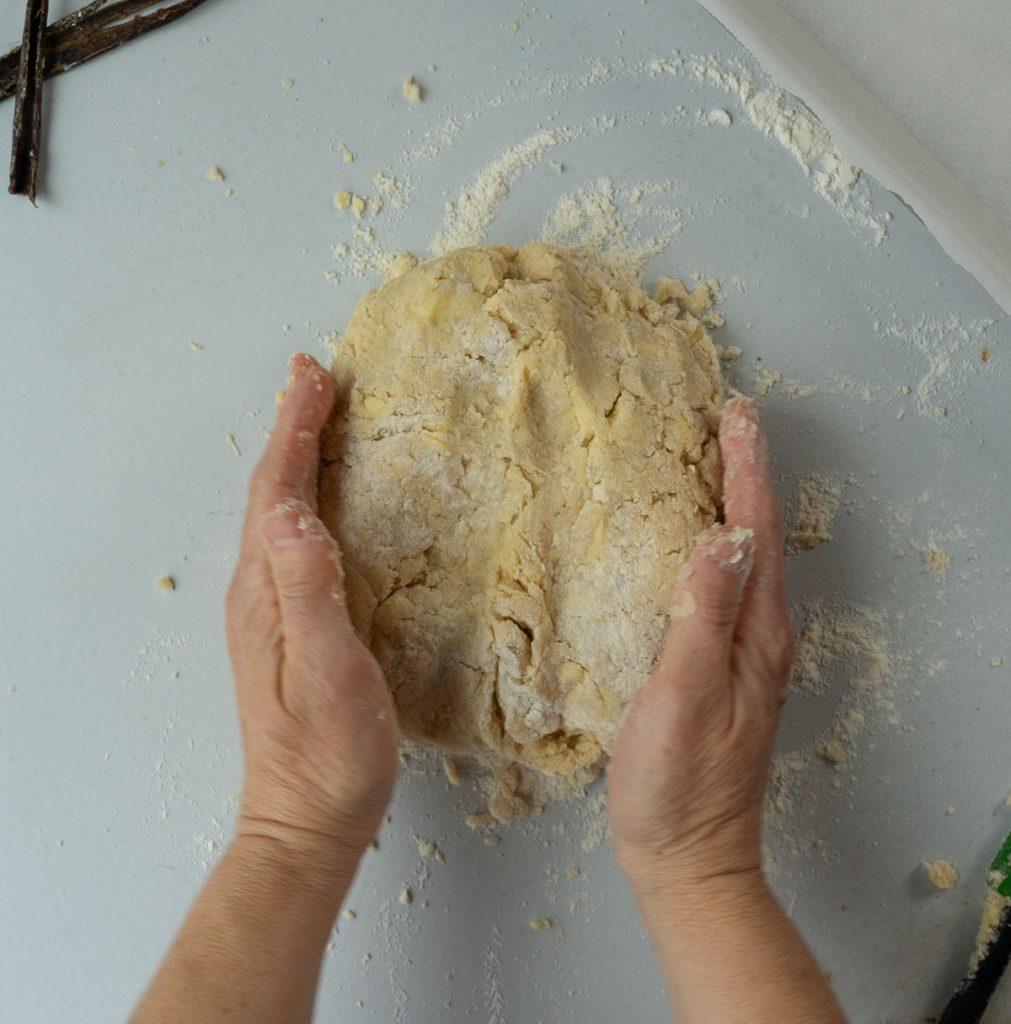 hands working scone dough into a round on a floured countertop