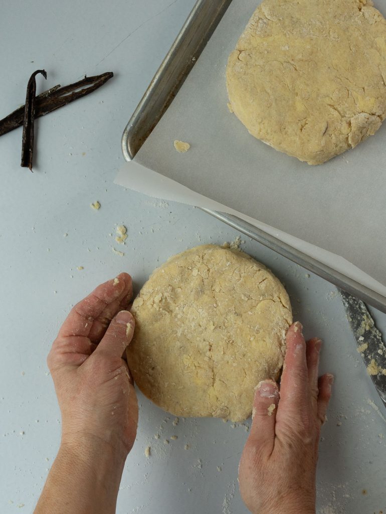 two scone rounds one is on a baking sheet the other is being shaped by hands