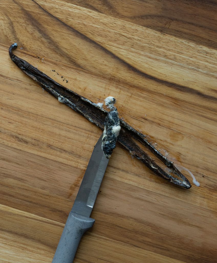 scraping seeds from vanilla pot with a pairing knife on a wood cutting surface