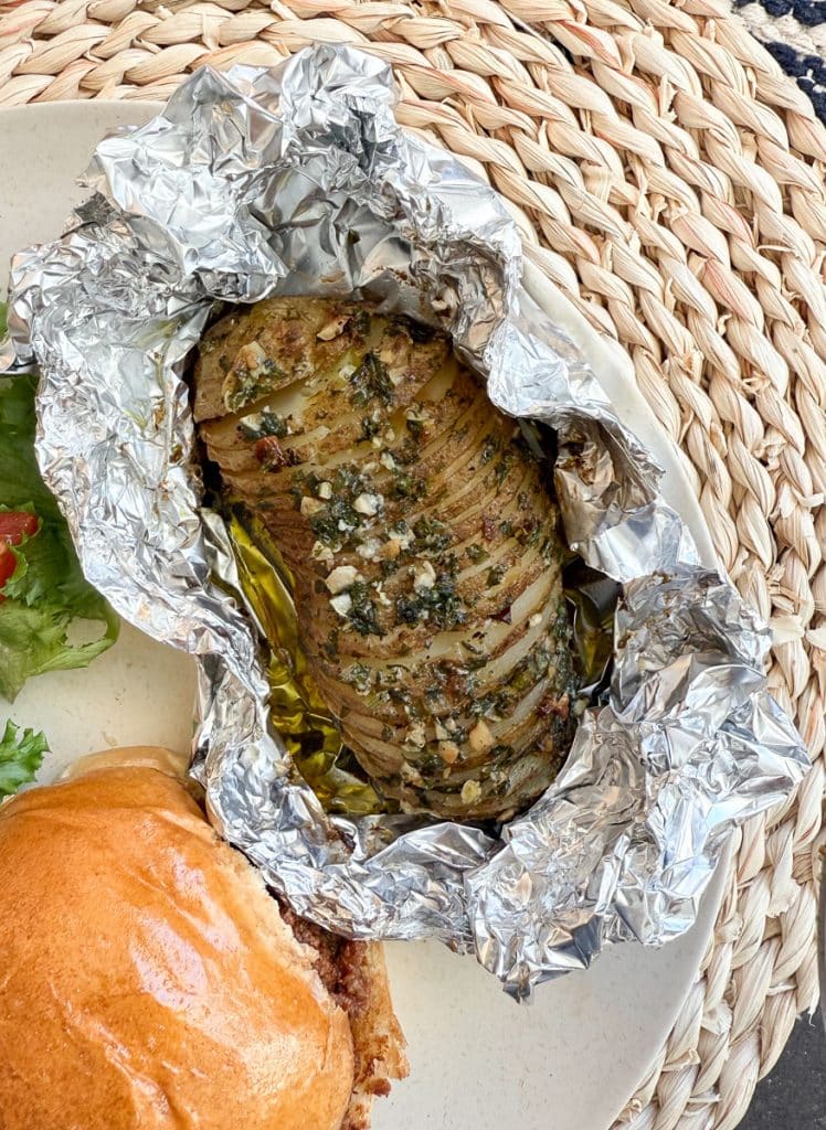 baked hasselback potato in the foil on a plate next to a sloppy joe