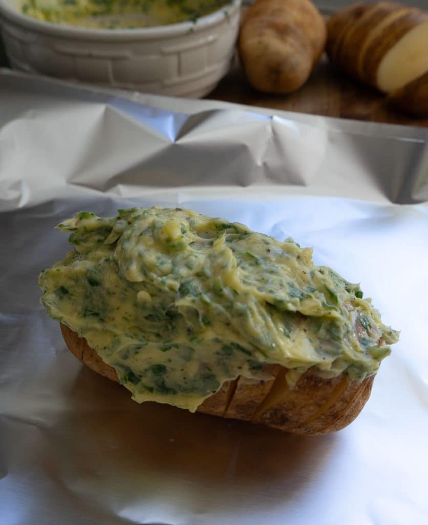 hasselback potato on aluminum foil covered with garlic herb butter