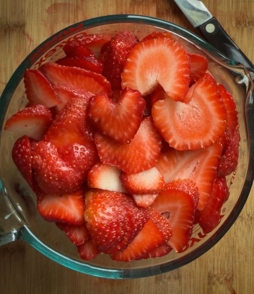 measuring cup full of sliced strawberries on a wood cutting board
