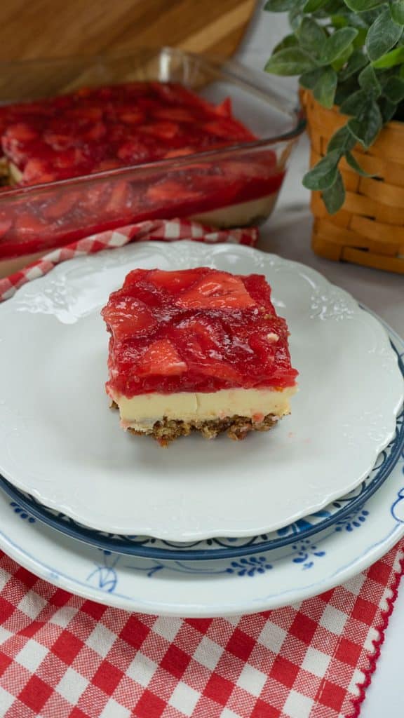 side view of a slice of strawberry cheesecake with a pretzel crust on a white dessert plate