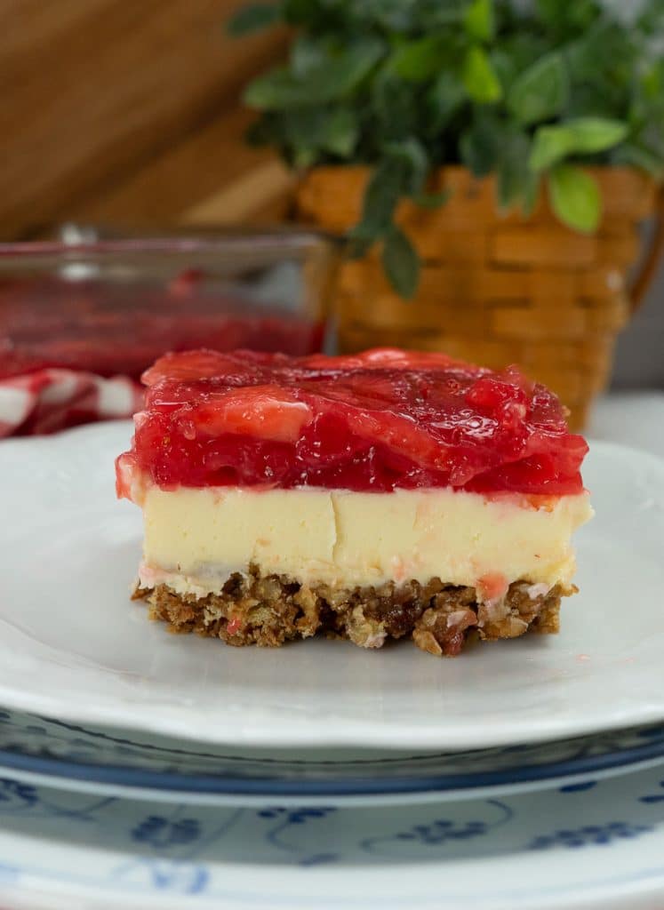 side view of a slice of strawberry cheesecake with a pretzel crust on a white dessert plate