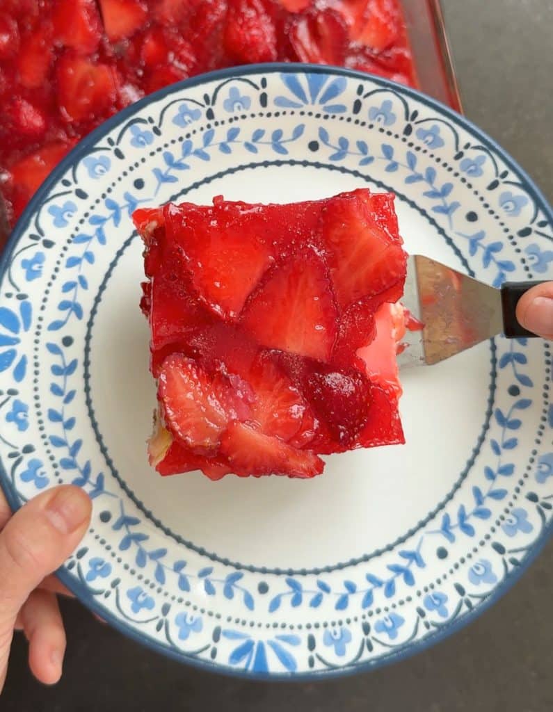 spatula placing a piece of strawberry cheesecake with pretzel crust on a dessert plate