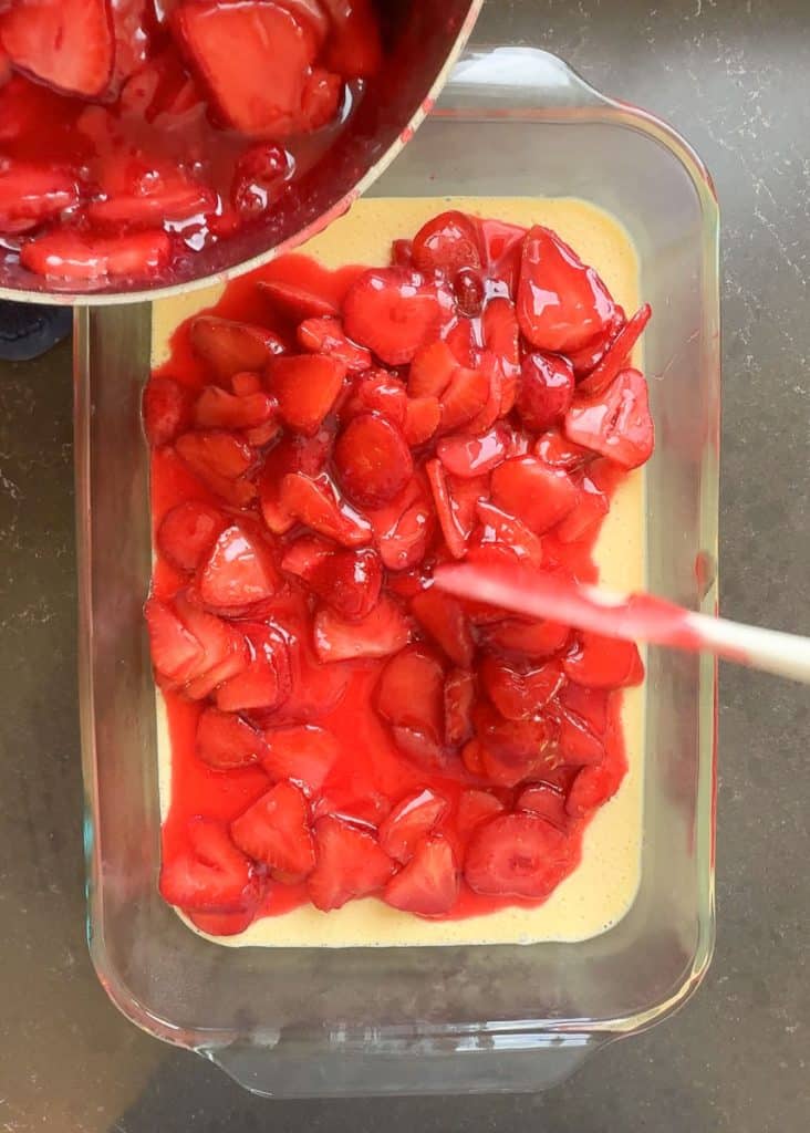 pouring strawberry topping over cheesecake layer