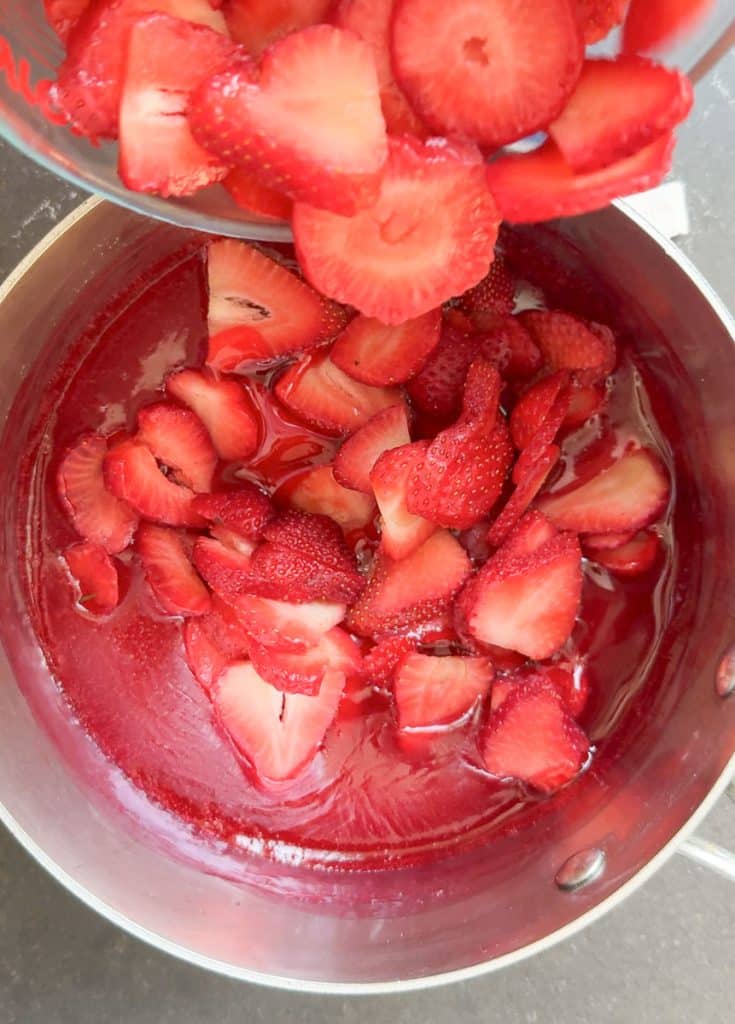 adding sliced strawberries to cooled strawberry gelatin
