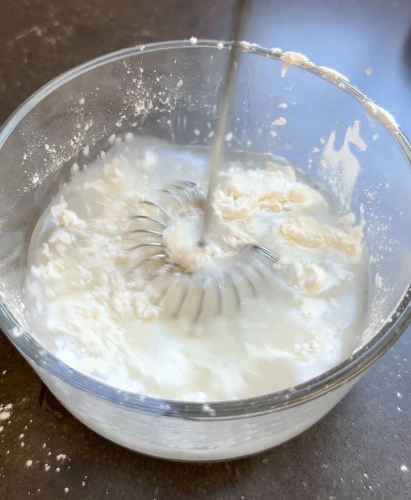 whisking together cold water and cornstarch in a clear glass dish on black countertop
