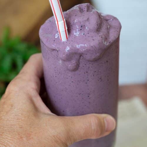 hand holding a smoothie with smoothie dripping down the side of the glass with a straw sticking out of the glass