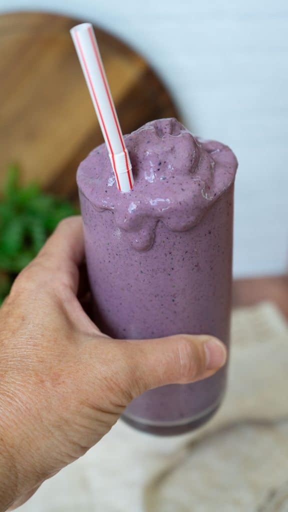 hand holding a smoothie with smoothie dripping down the side of the glass with a straw sticking out of the glass