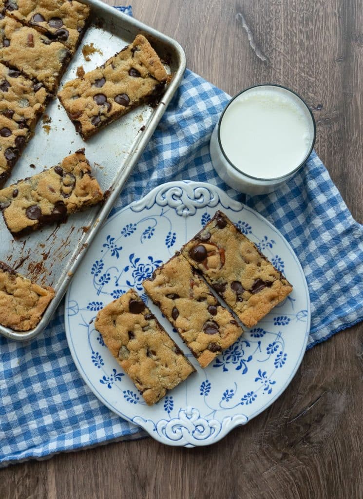 plate of caramel pretzel chocolate chip cookie bars on a plate with a glass of white milk next to the whole pan of cut cookie bars