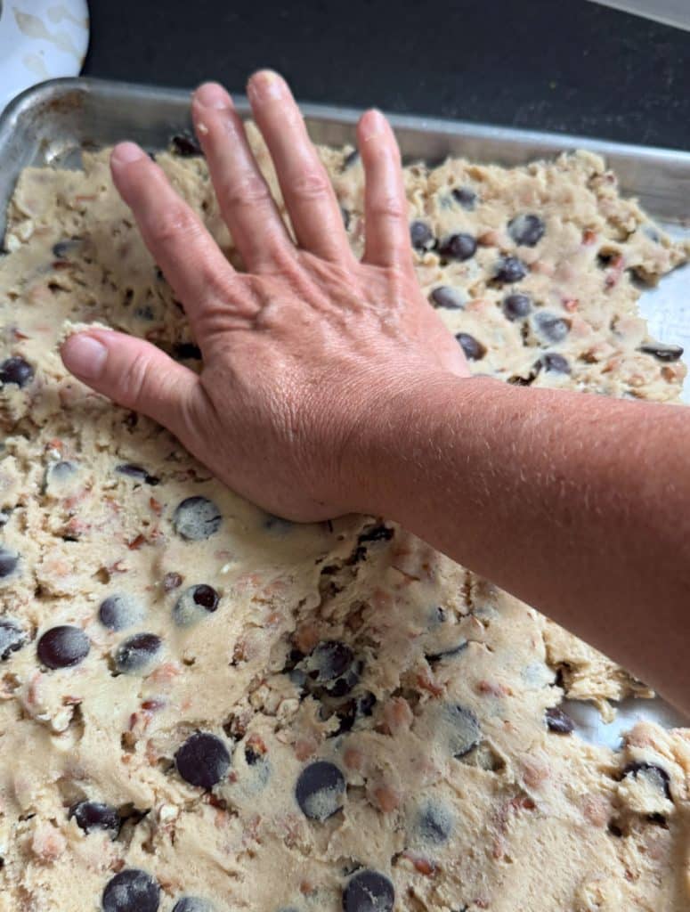 pressing cookie dough into baking sheet with the heal of hand