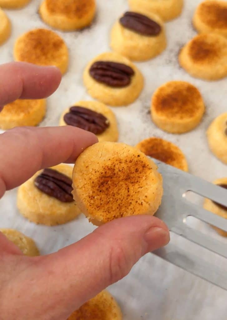 hand holding a baked cheese cracker over baking sheet of crackers