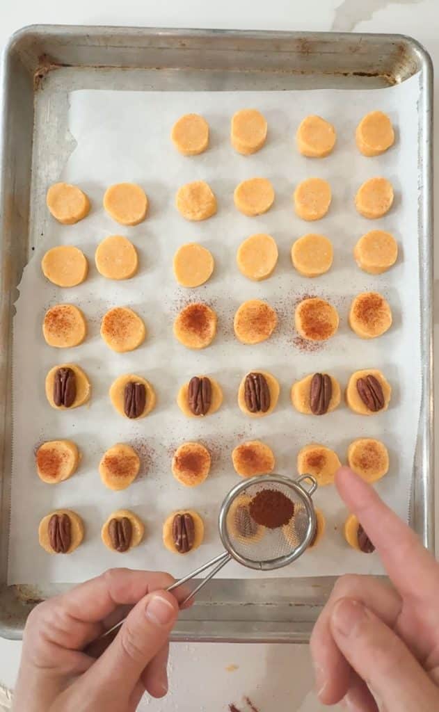 cheese cracker discs on a parchment lined baking sheet. hands are dusting crackers with smoked paprika through a sieve