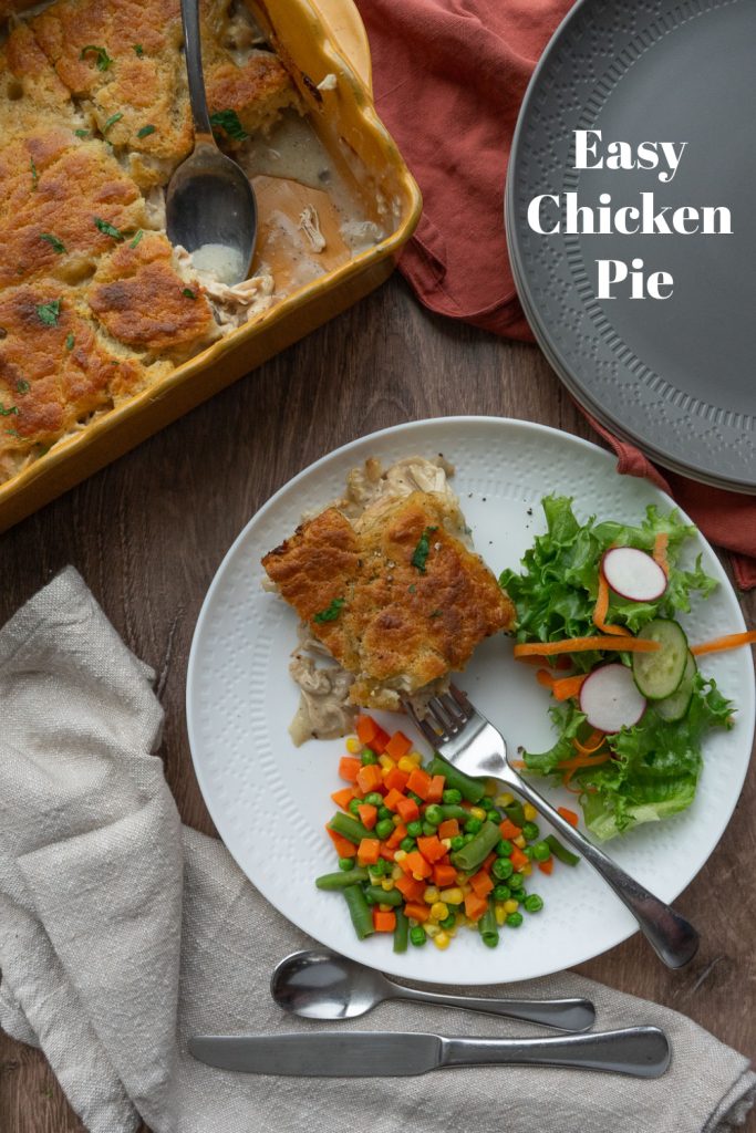 chicken pie on a white plate with mixed veggies and a salad casserole dish is to the top of the plate of food