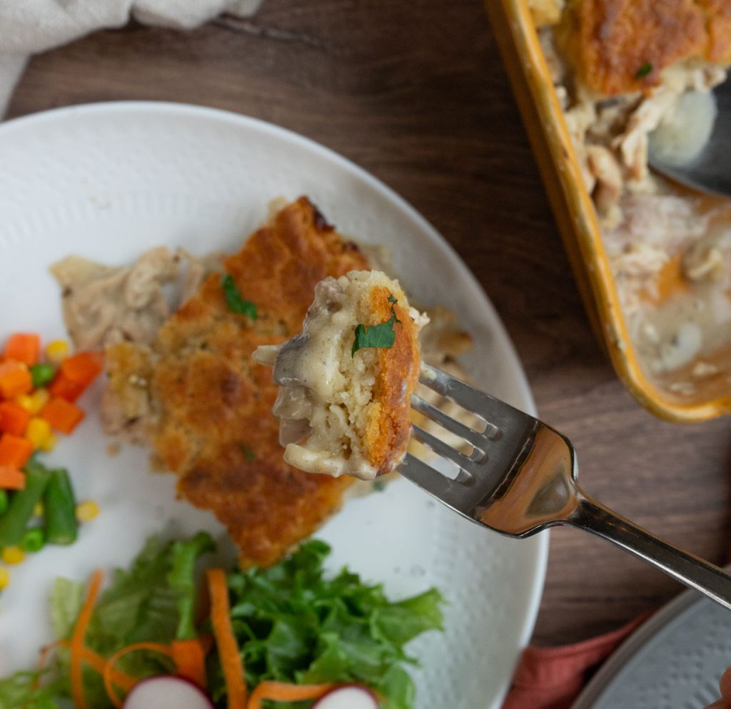 fork with chicken pie on it, plate of chicken pie, veggies and salad in the background