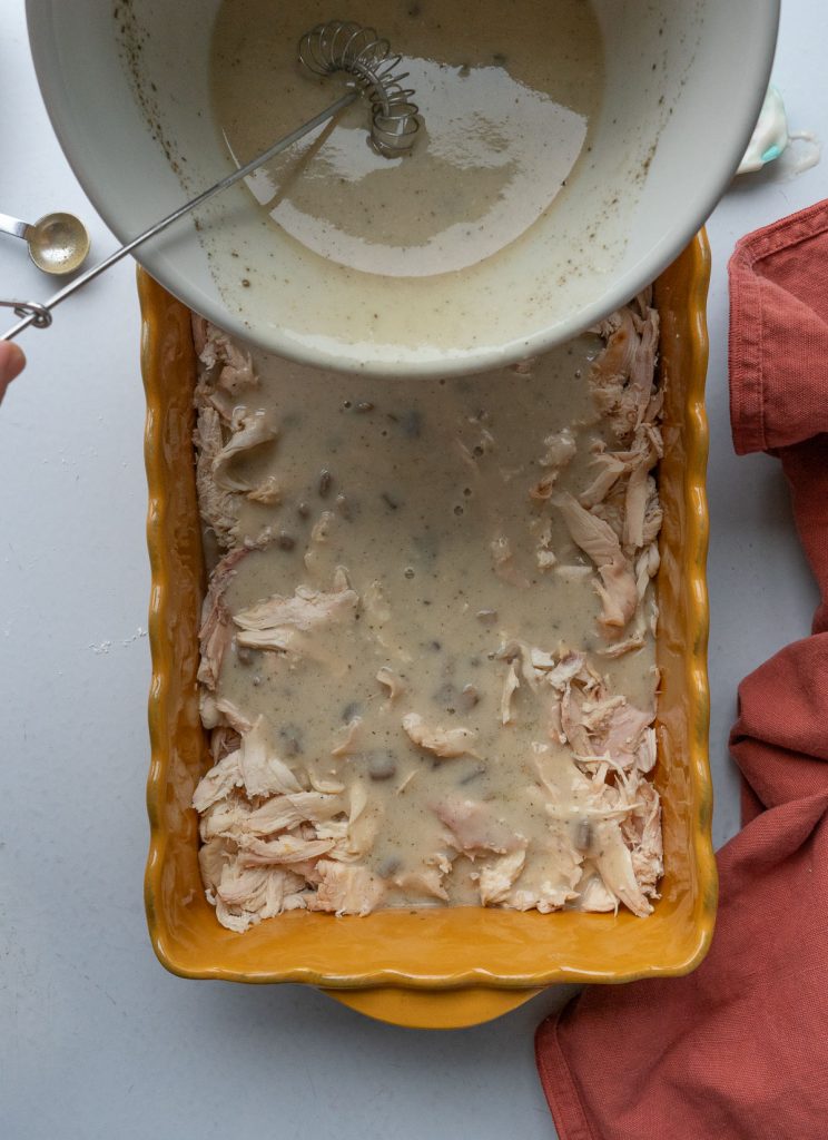 pouring sauce over the chicken that is in a casserole dish. 