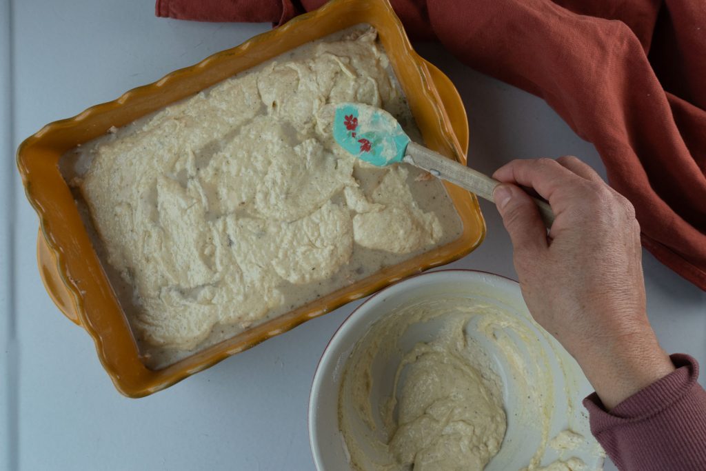 spooning crust batter over the chicken and sauce mixture in a yellow casserole dish