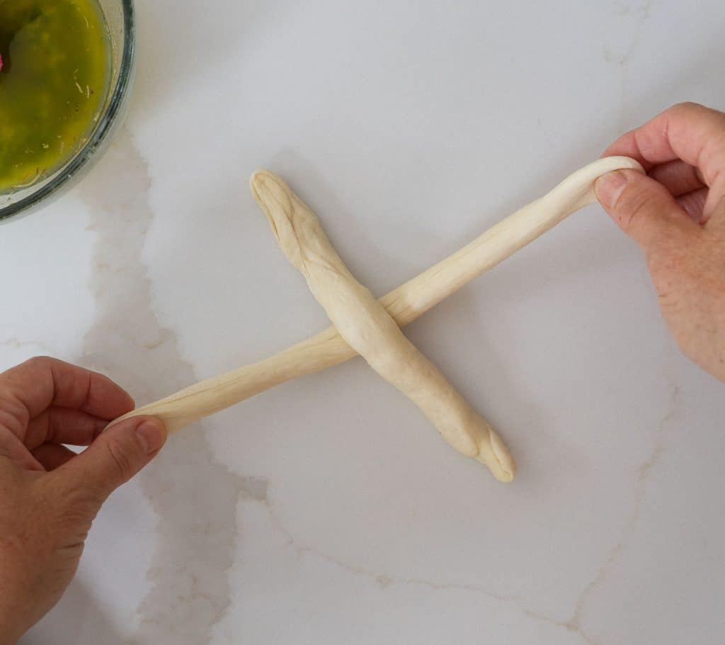 making a cross out of the two dough sticks on the white countertop. hands are holding the end of one of the sticks