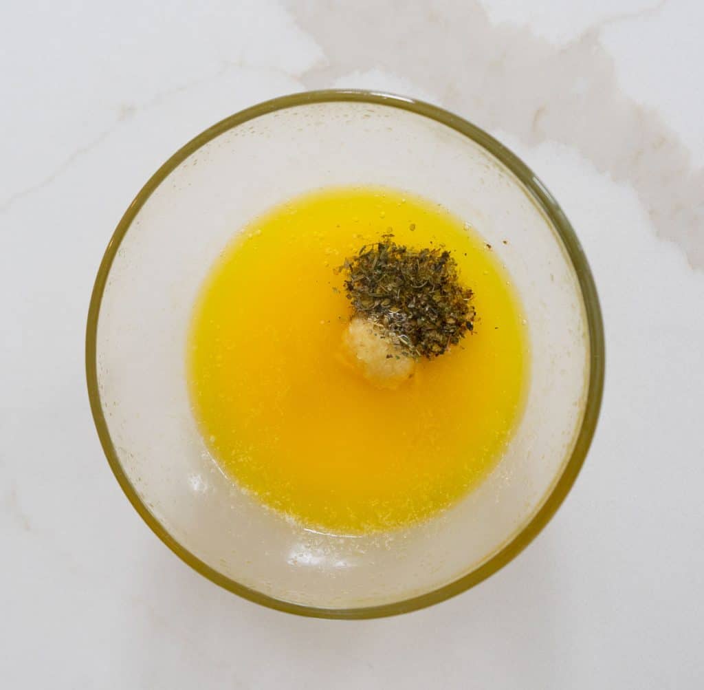 melted butter, garlic and other seasonings in a glass bowl on white countertop
