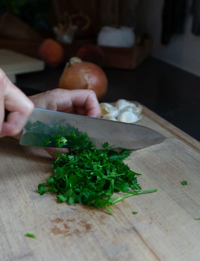 chopping fresh herbs and mincing garlic on a wood cutting board