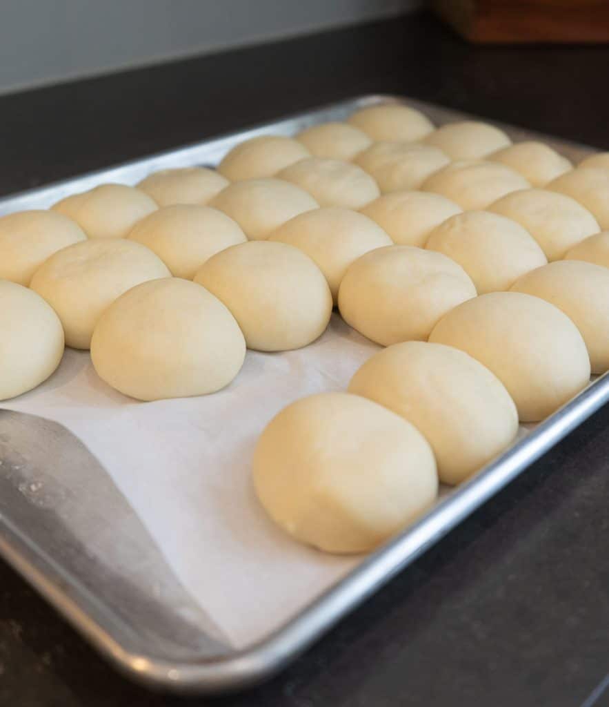 frozen dinner rolls thawing and rising on a baking sheet lined with parchment paper on kitchen counter top