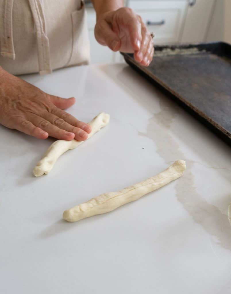 rolling rolls out into log sticks on a white counter top