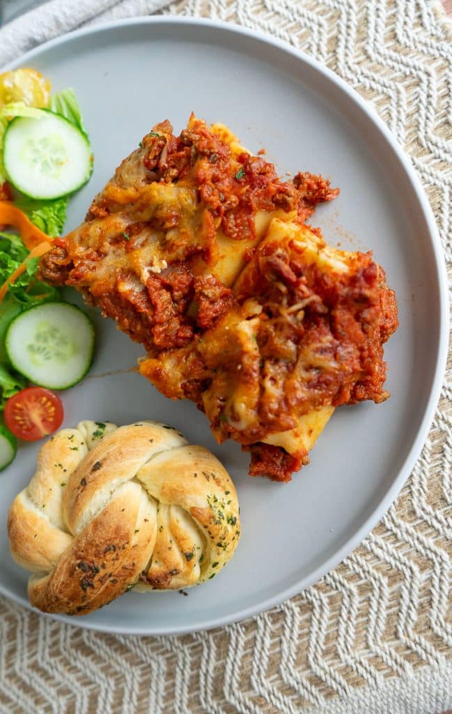 lasagna rollups on a gray plate with a garlic knot and  and salad on a tan place mat