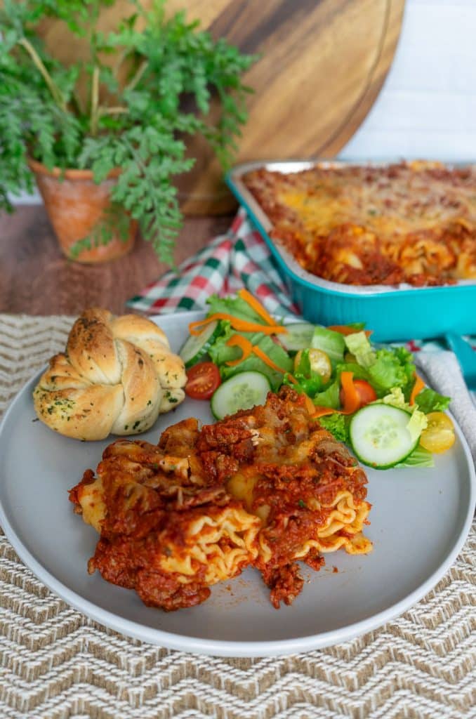 lasagna rollups on a gray plate with a garlic knot and and salad on a tan place mat
