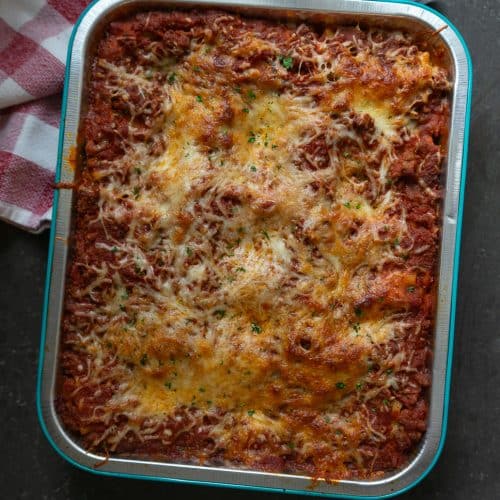 pan of baked lasagna roll ups sitting on black countertop with a red and white towel in the upper lefthand corner of the photo
