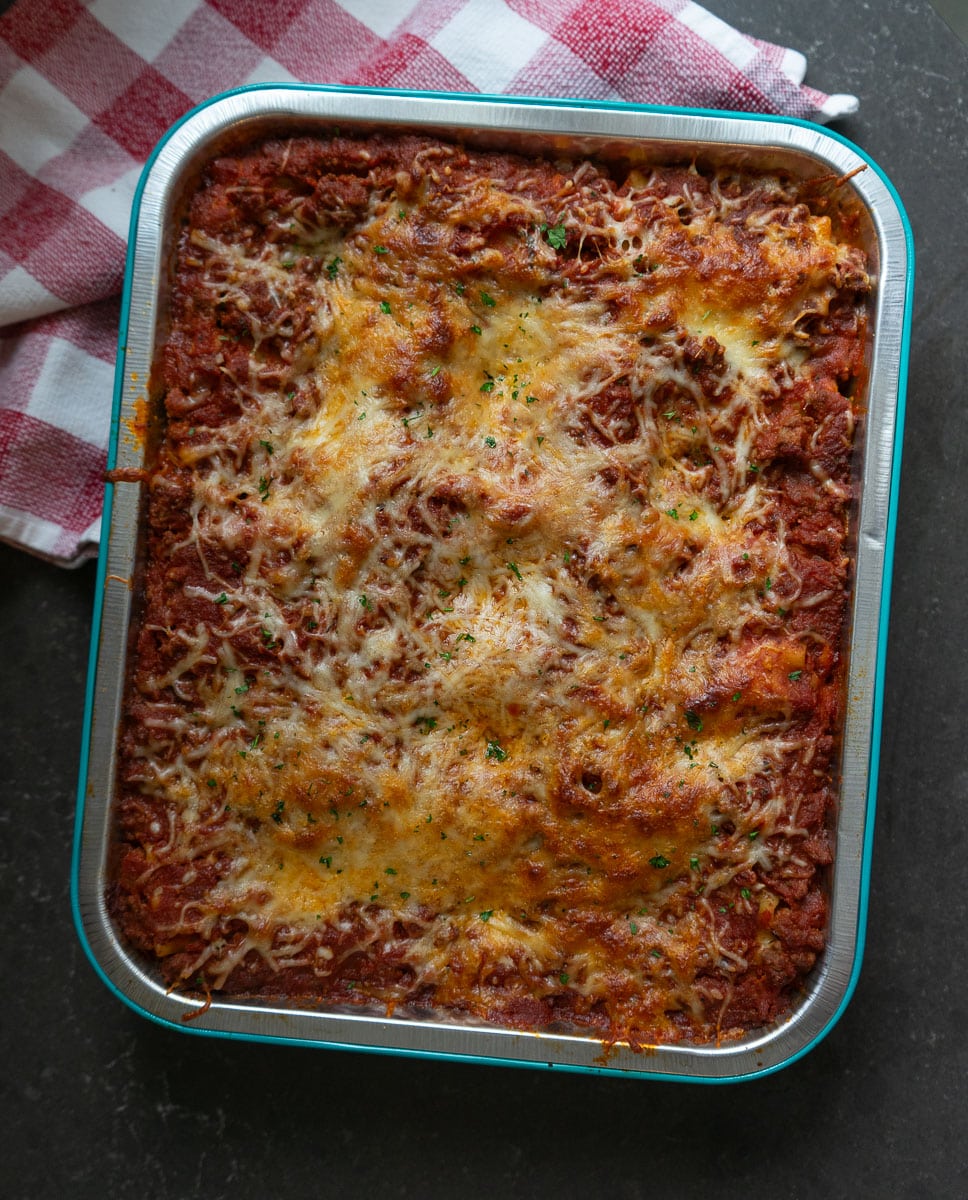 pan of baked lasagna roll ups sitting on black countertop with a red and white towel in the upper lefthand corner of the photo