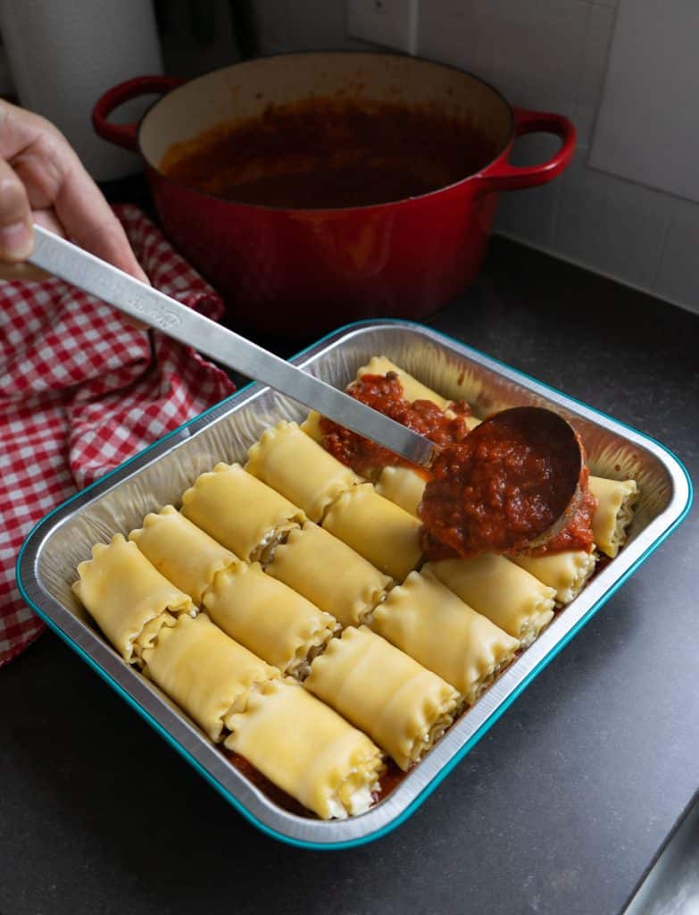 ladle spooning sauce over lasagna roll ups in a 9x13 pan