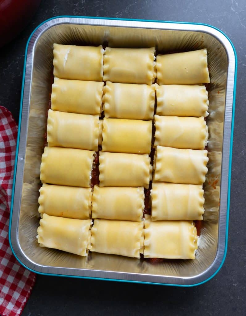 lasagna noodles filled with cheese filling on top of the sauce in 9x13 pan