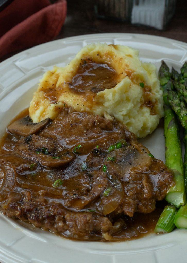 swiss steak on a plate with mashed potatoes and asparagus