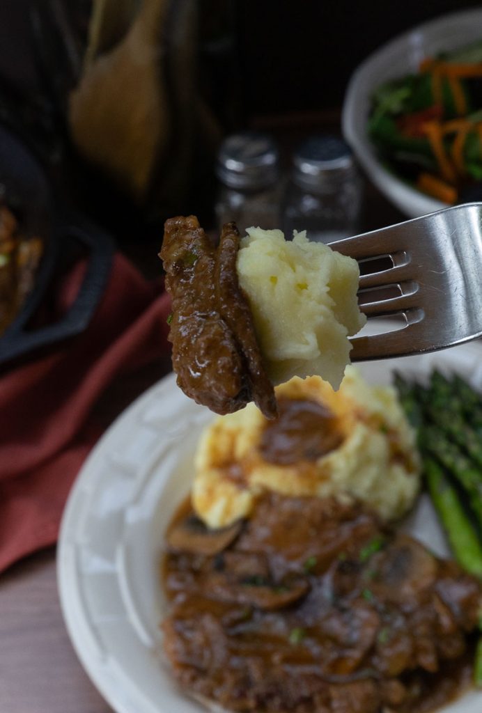 steak, gravy, and mashed potatoes on a fork with dinner plate in the back ground