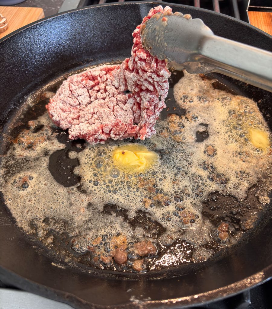 butter melting in a skillet tongs adding a steak to the cast iron skillet