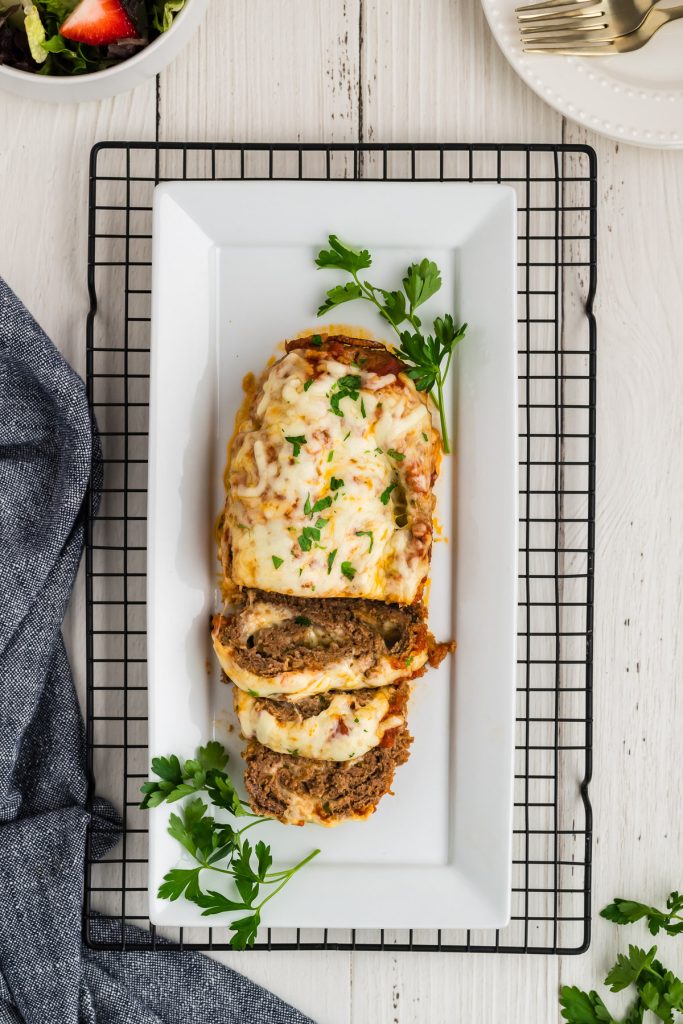 sliced italian meatloaf on a white platter that is sitting on a cooling wrack with parsley