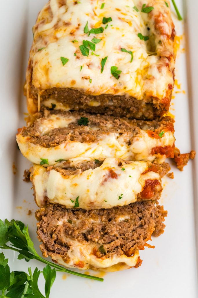 sliced meatloaf on a white platter with greens on the side