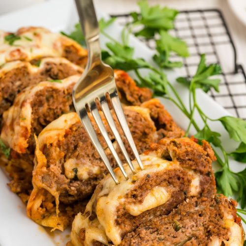 sliced meatloaf on a white platter with a fork piercing the first slice of meatloaf