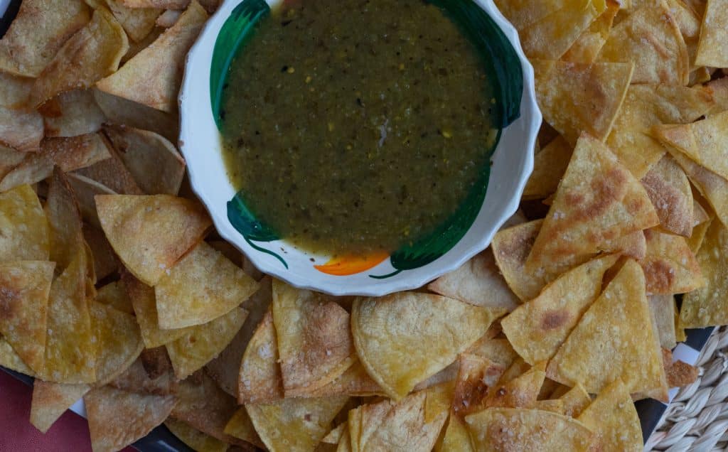 plate of corn tortilla chips with a bowl of salsa verde in the middle