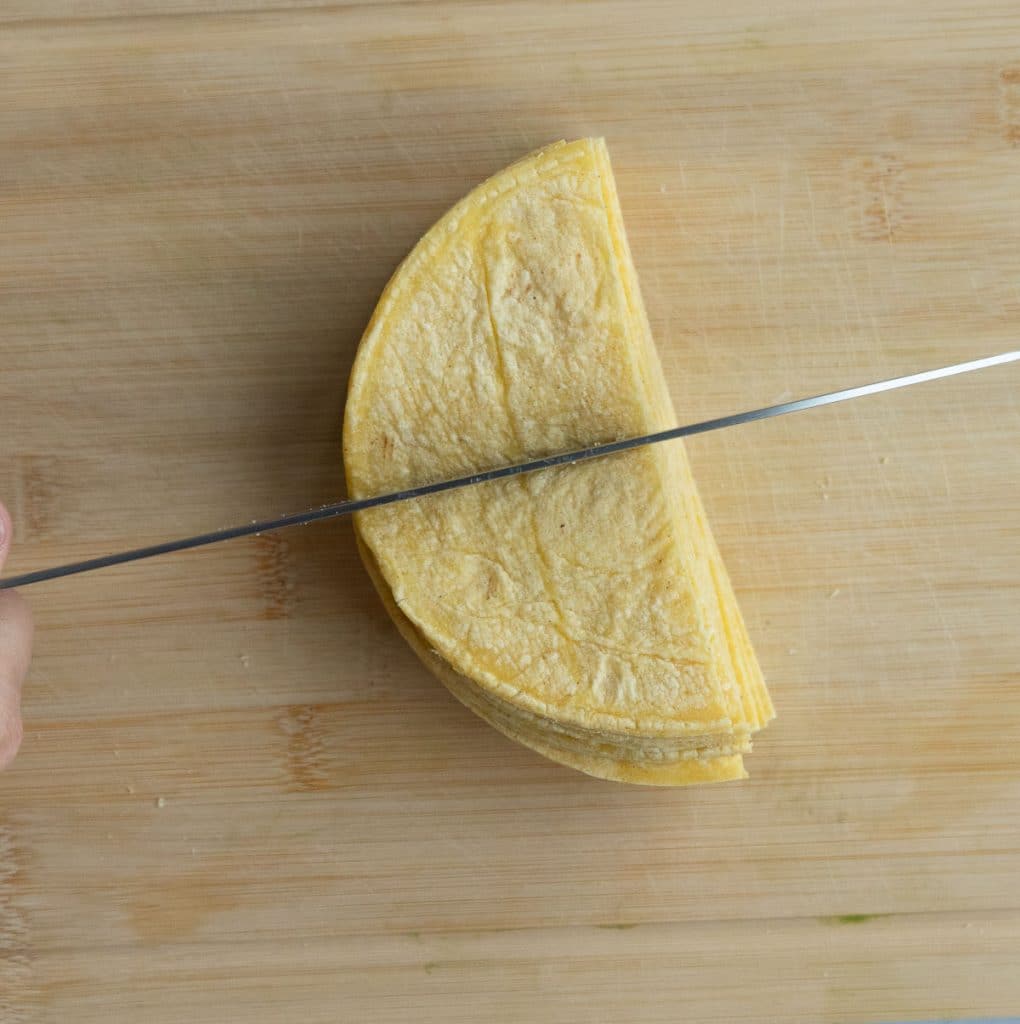 on a wood cutting board cutting corn tortillas in to triangles