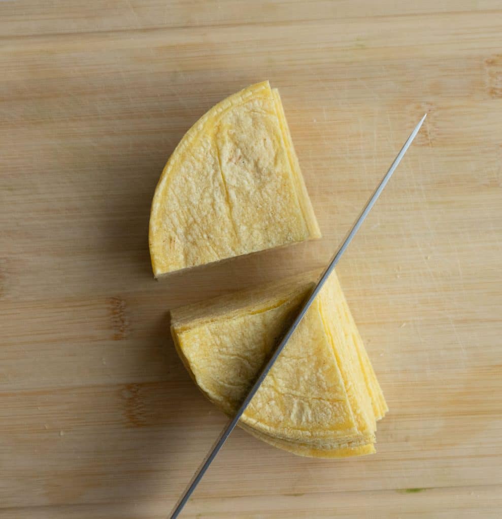 on a wood cutting board cutting corn tortillas in to triangles