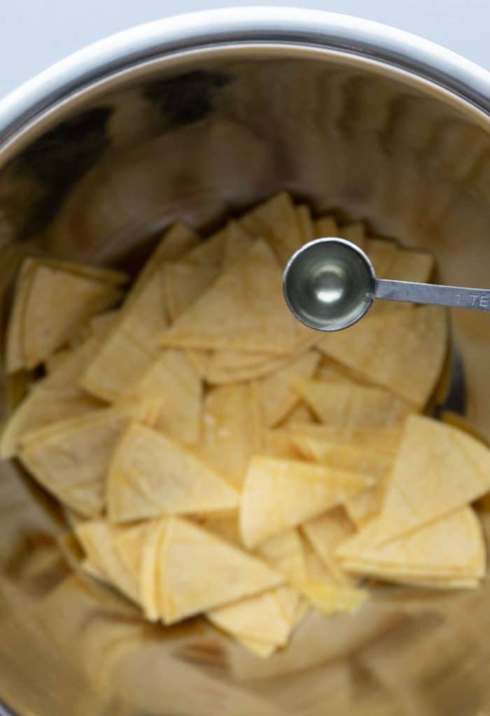 drizzling salt over corn tortilla wedges in a silver bowl