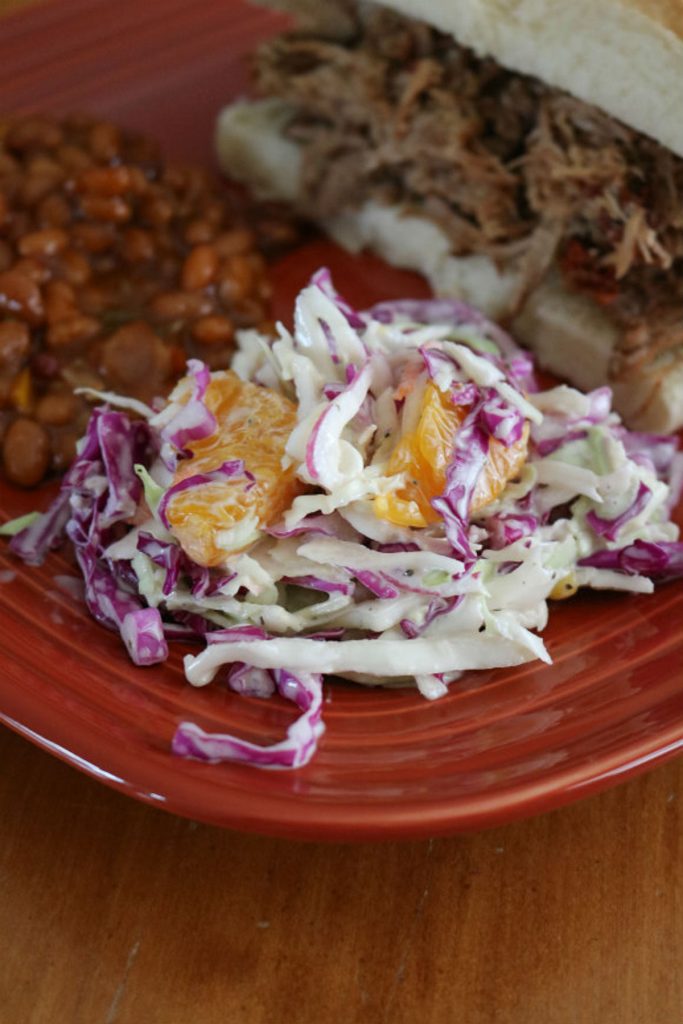 gulf coast coleslaw on a rust colored plate with baked beans and a sandwich in the background