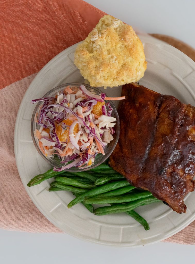 gulf coast coleslaw on a white plate with green beans, bbq ribs, and a biscuit