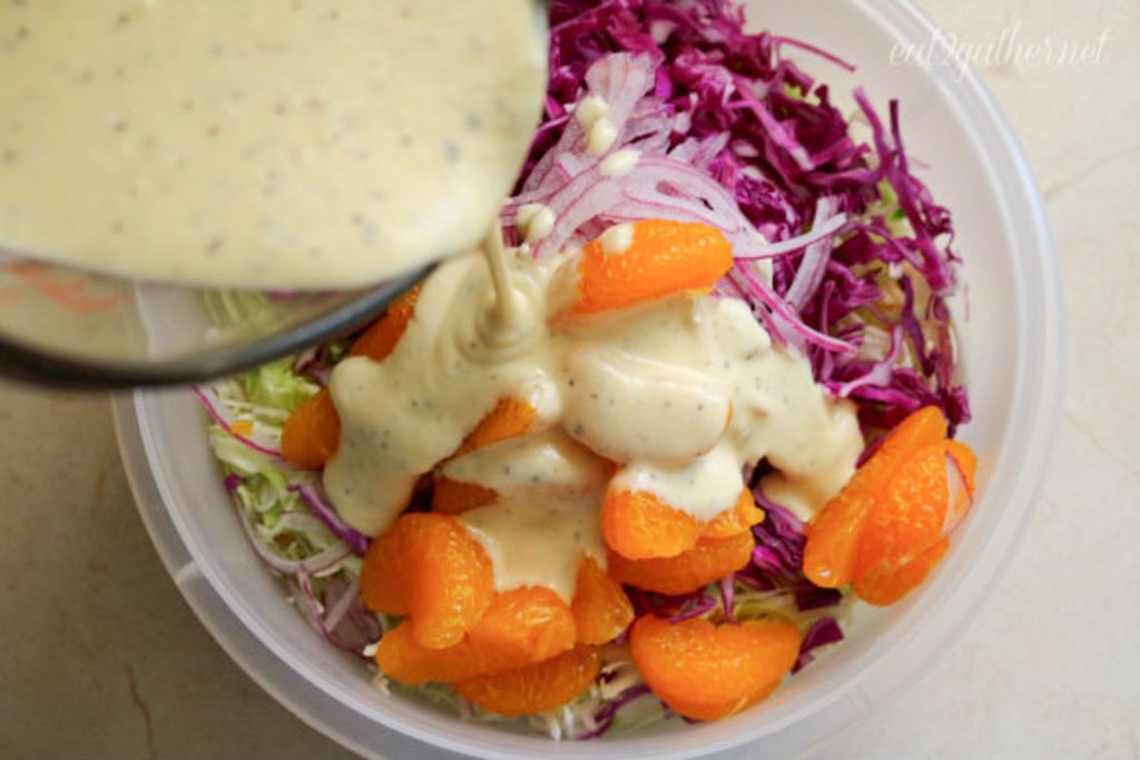 adding salad dressing to coleslaw ingredients, glass bowl is in upper left hand corner pouring dressing on coleslaw