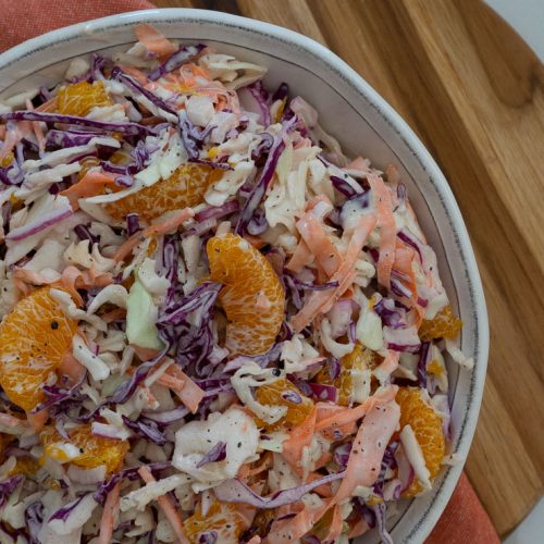 white bowl with gulf coast coleslaw in it, on a round cutting board on a white countertop