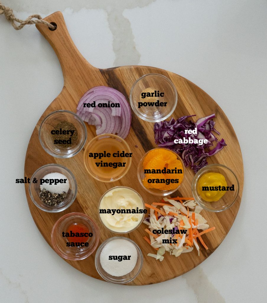 gulf coast coleslaw ingredients in small bowls on a round wood cutting board on a white countertop