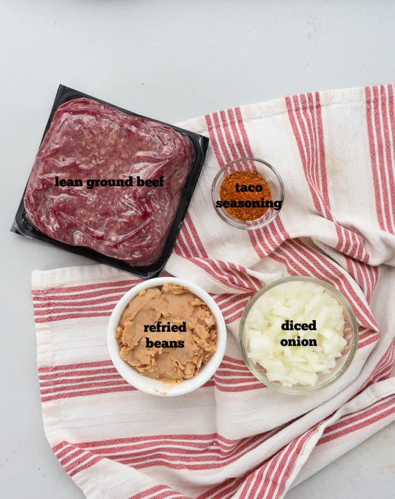 ingredients for the burrito meat filling laid out on a white countertop with a red and white striped towel