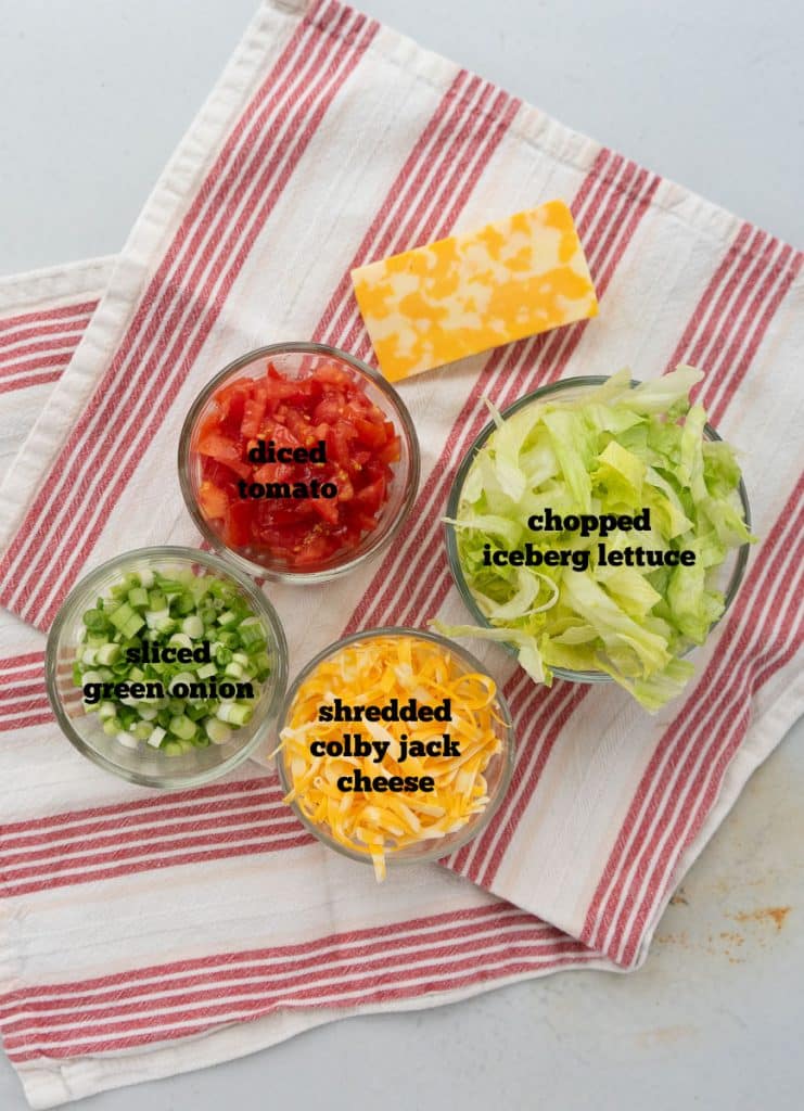toppings or extra fillings for wet burritos on a white countertop with a red and white striped towel